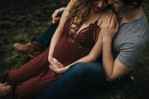 pregnant couple snuggling in forest