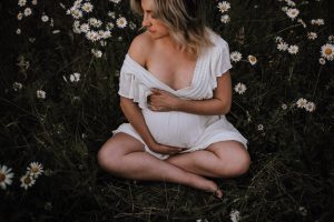 pregnant woman sitting in daisy field