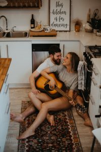 couple playing guitar while sitting on kitchen floor