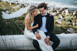 married couple sitting on a log by the ocean