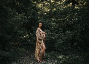 pregnant woman standing in the forest with her bare belly showing