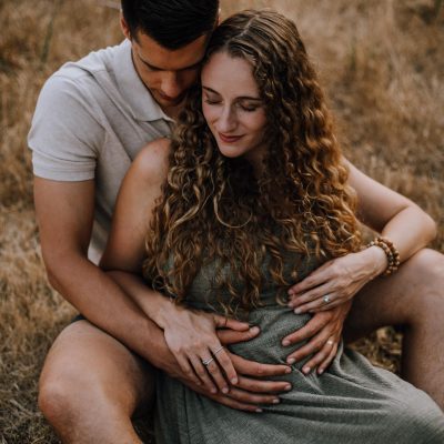 pregnant couple snuggling the tall grass